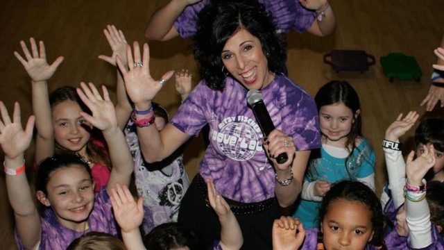 Woman in purple shirt engaging with excited children at event.