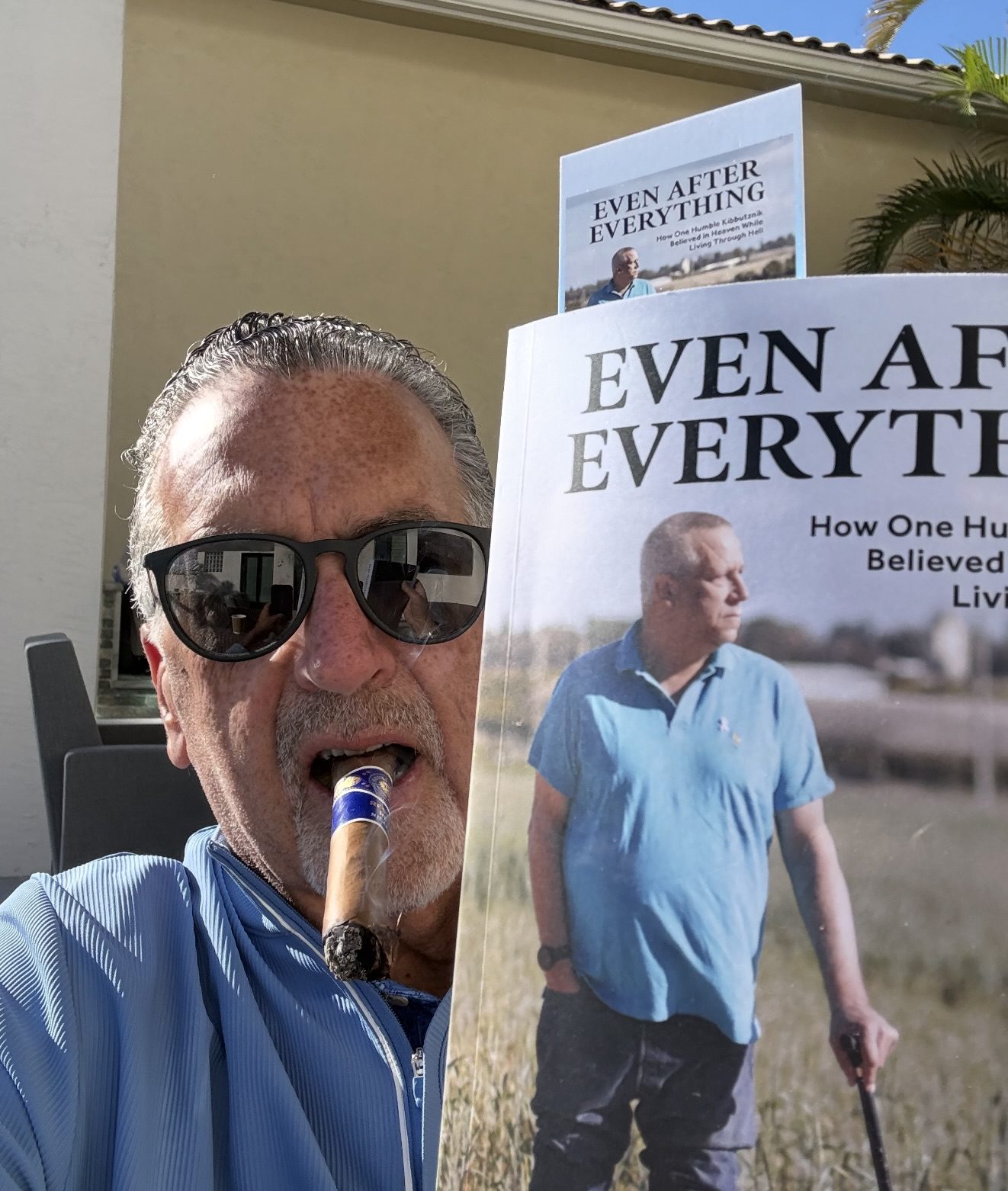 Man with sunglasses and a cigar holding a book titled 'Even After Everything'.
