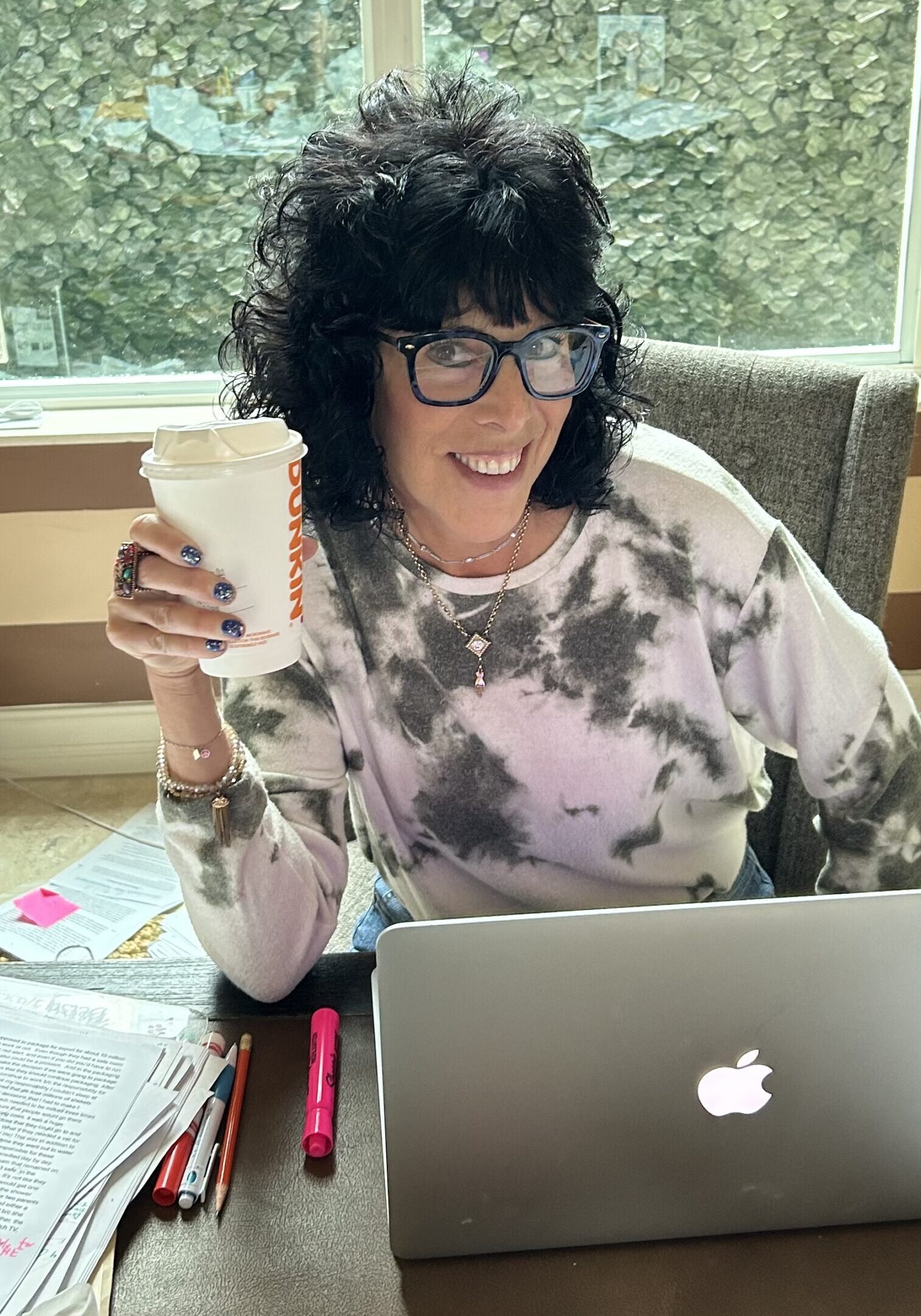 Woman smiling and holding a coffee cup while working on a laptop.