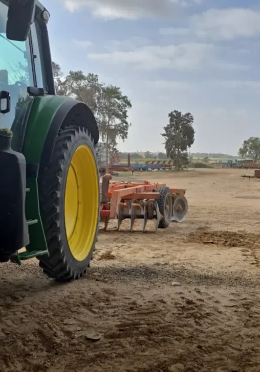 Tractor working on dry farmland under a partly cloudy sky.