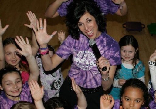 Woman in purple shirt engaging with excited children at event.